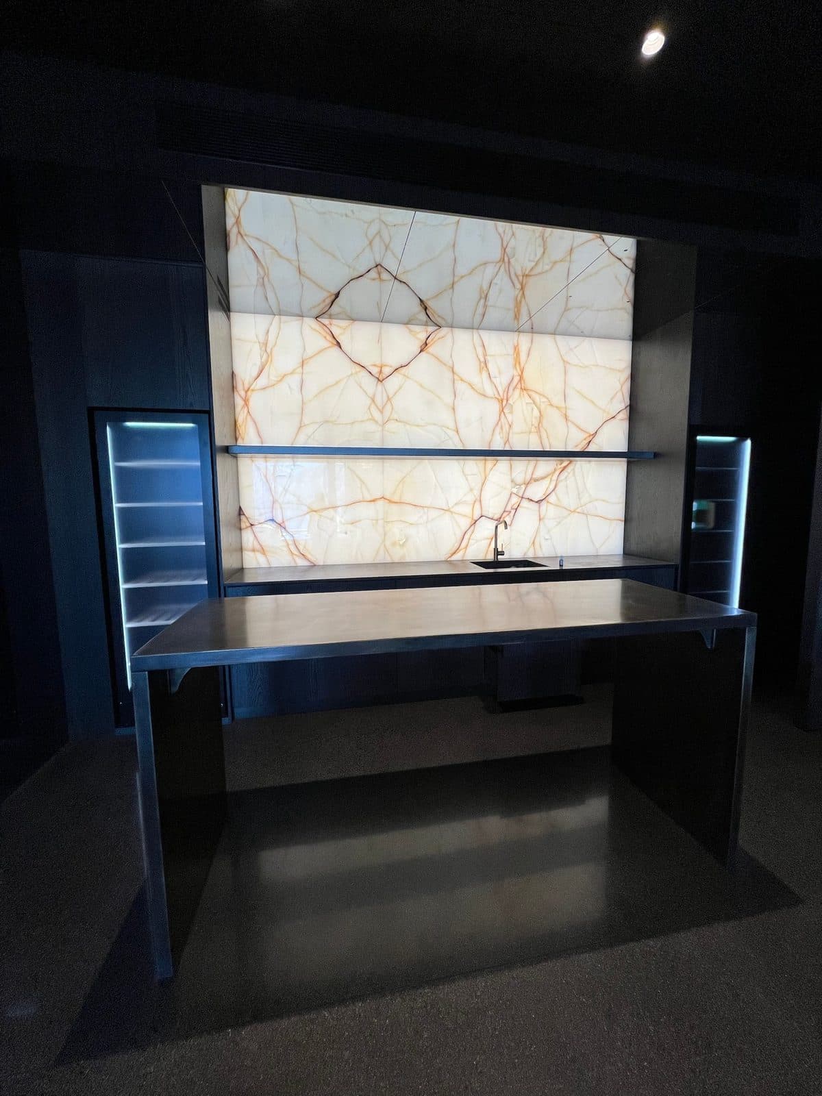The bar centred on the onyx wall with lit cabinets either side