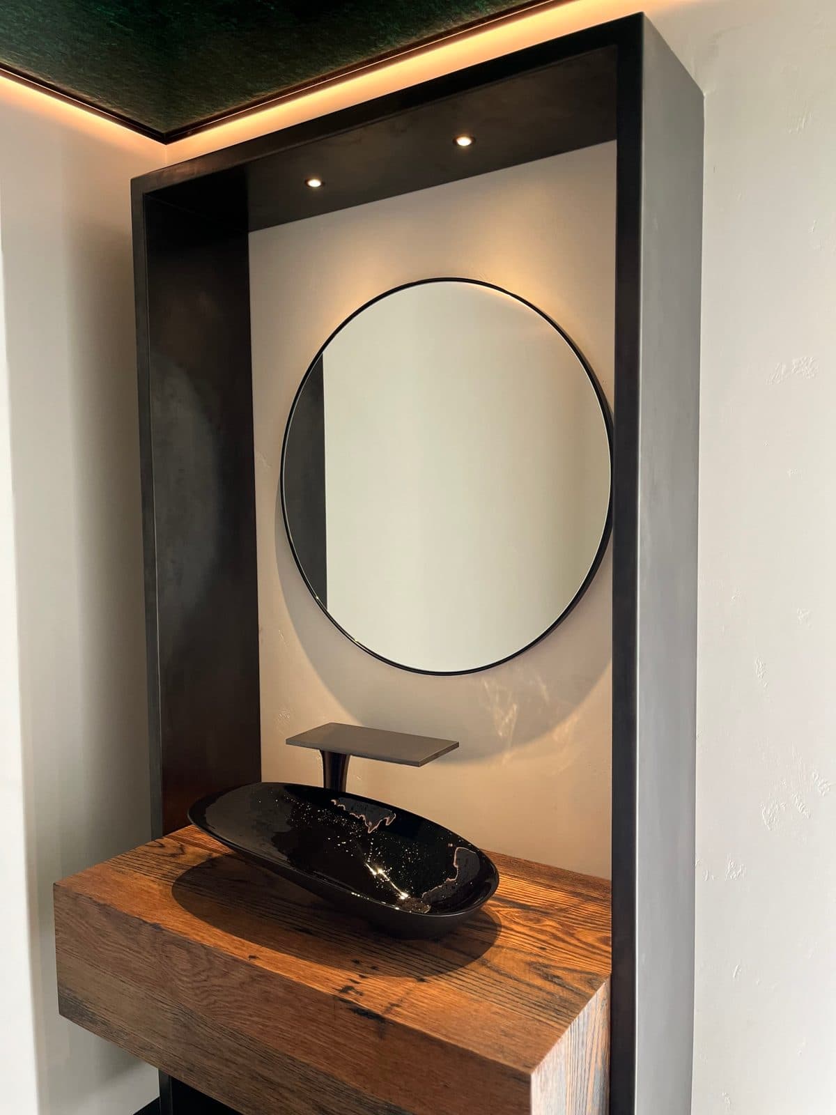 Round black mirror inside a blackened steel niche above an oak vanity