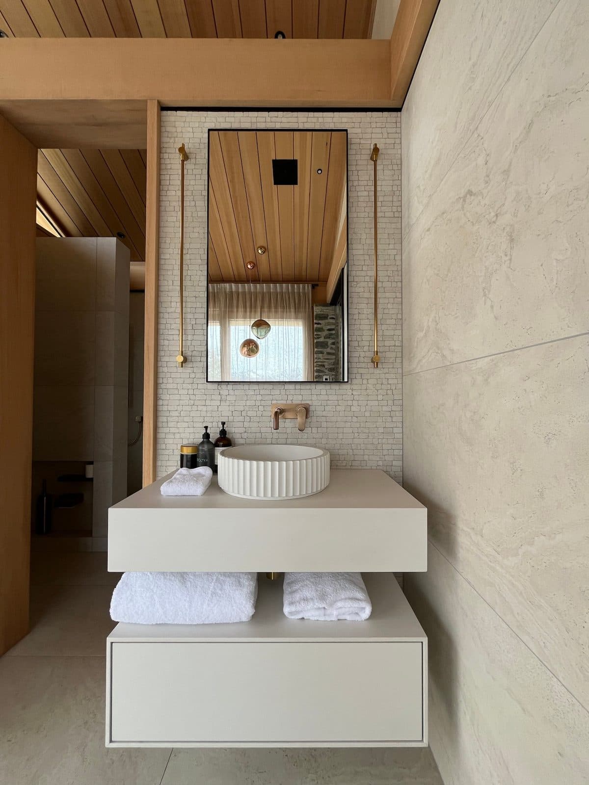 Black-framed rectangular mirror between two brass rails above a fluted basin