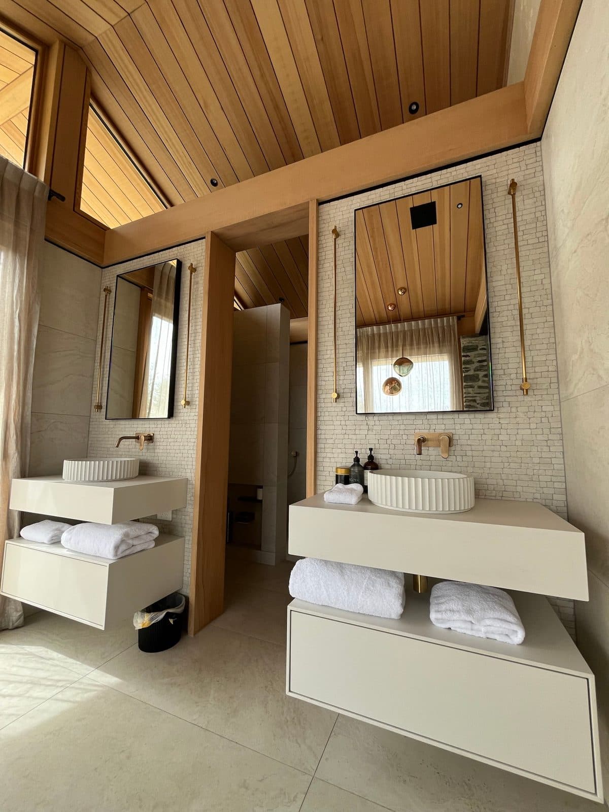 Twin floating vanities with black mirrors and brass rails under a timber ceiling