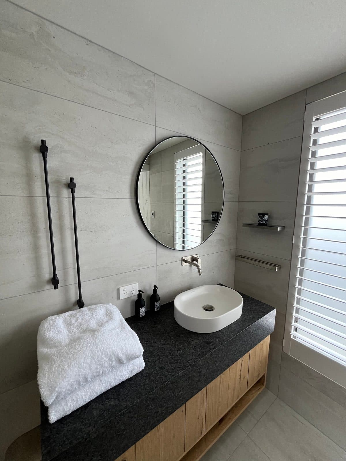 Round black mirror over a white basin with black towel rails