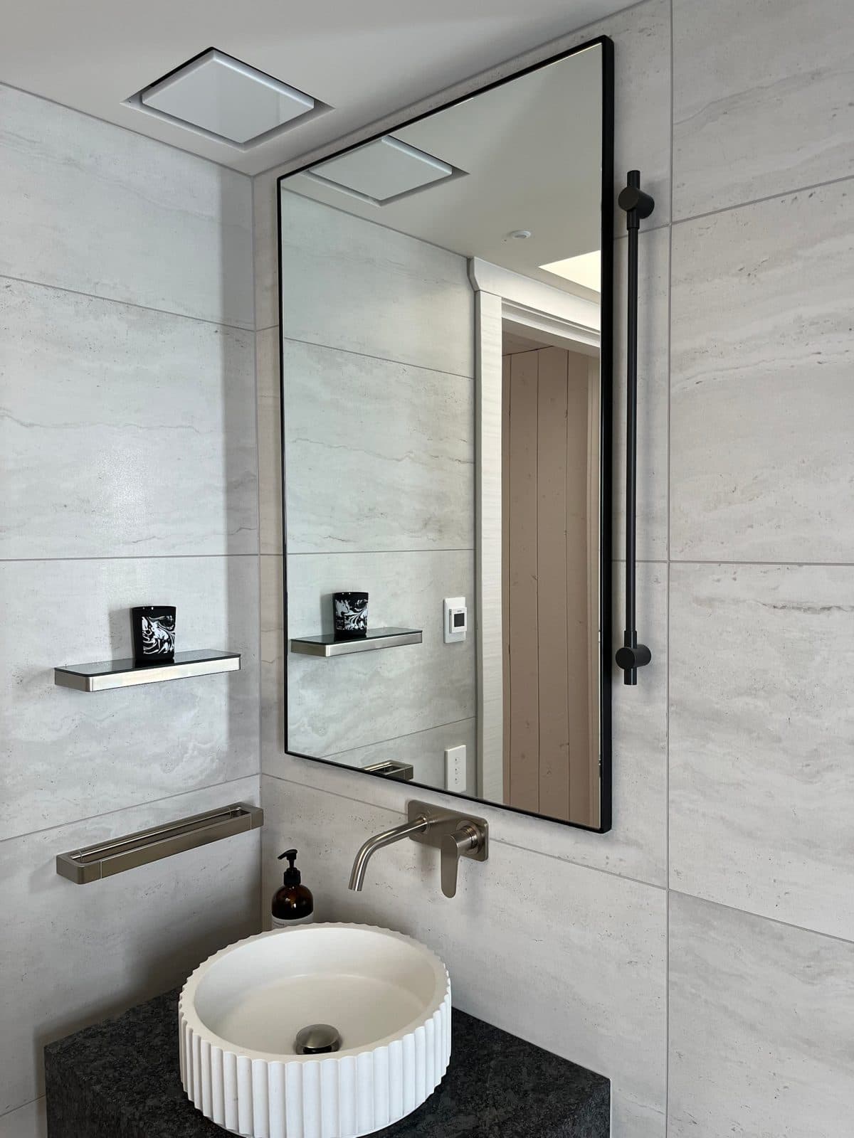Tall black rectangular mirror with a black rail over a fluted basin