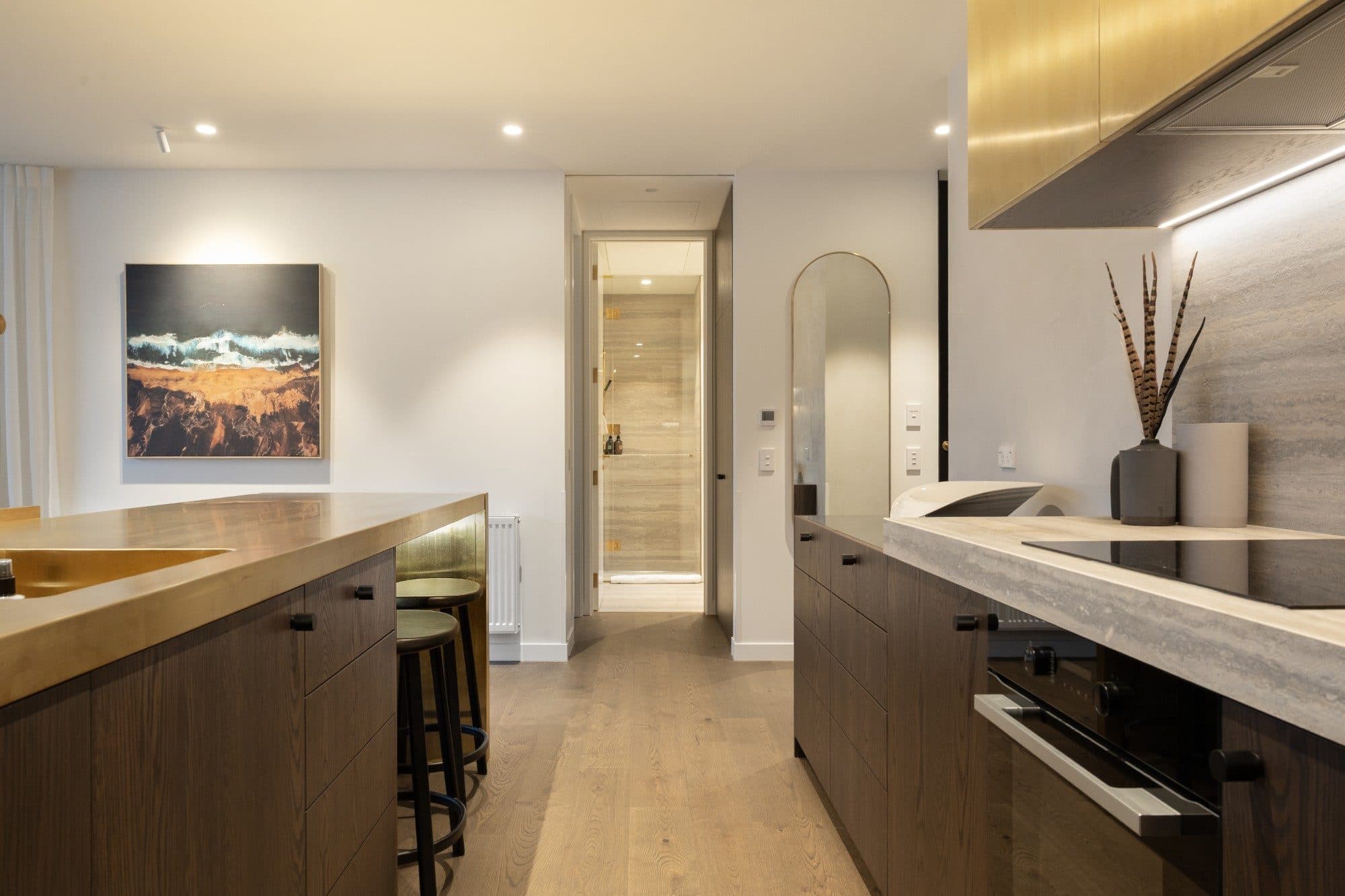Kitchen with a brass splashback and a brass pill mirror in the hallway